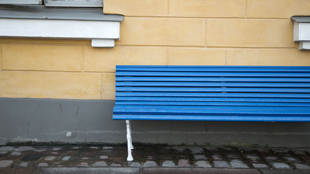 En blå bänk framför en gul byggnad.