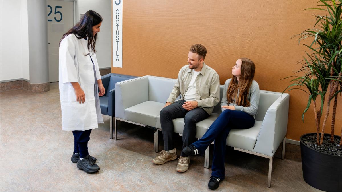 Kuvassa lääkäri keskustelee odotusaulassa odottavien kahden henkilön kanssa.