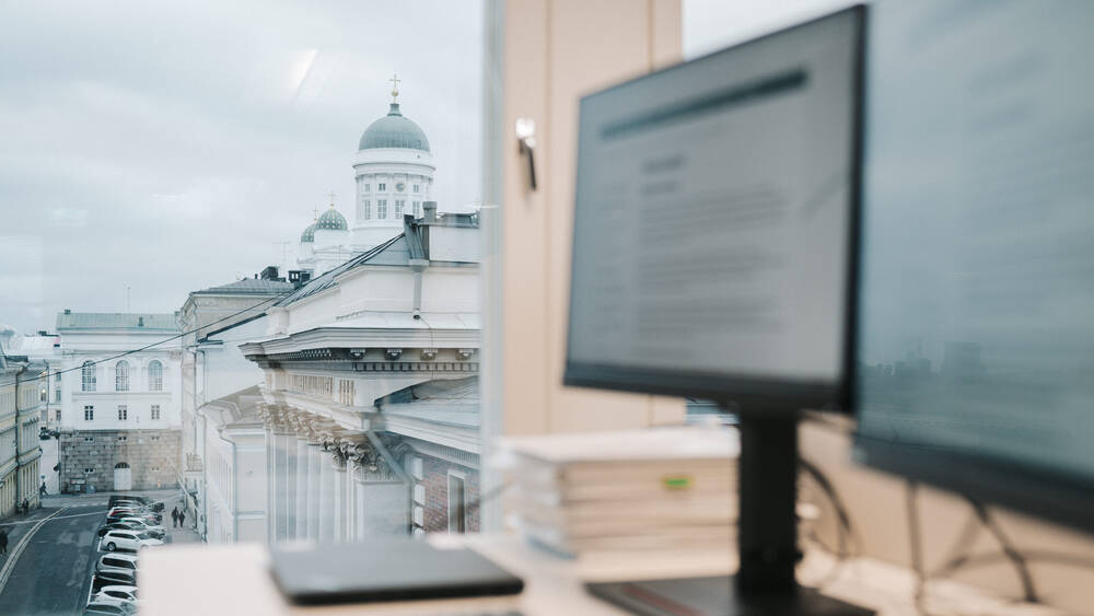 Kuvassa tietokoneen näyttö ja taustalla Helsinkiä